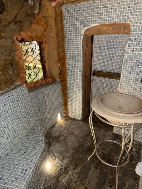 Bagno turco in stile rustico con piastrelle, lavandino e panca illuminata.